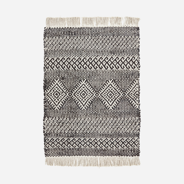 Black and white patterned rug with fringes on a light gray background